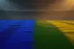 Empty floodlit stadium pitch at golden-hour kick-off with blue and green-yellow shadow patterns, no players