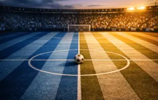 Aerial floodlit stadium view with sky-blue and white pitch markings, golden-hour lighting, and a football on centre spot.