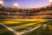 Floodlit stadium with colourful bunting, packed stands, and shadow-dappled pitch at golden hour.