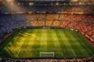 Overhead view of floodlit stadium with colourful flag-draped sections and long shadows across pitch during group-stage pre-match atmosphere.