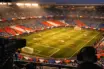 Floodlit stadium bowl with bunting in national colours, shot from broadcast gantry at golden hour.