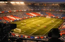 Floodlit stadium bowl with bunting in national colours, shot from broadcast gantry at golden hour.