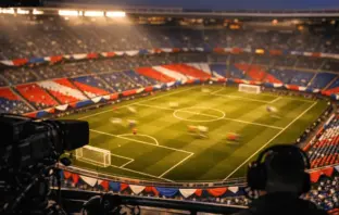 Floodlit stadium bowl with bunting in national colours, shot from broadcast gantry at golden hour.