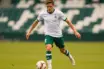 Young midfielder in white and green kit dribbling football on professional pitch