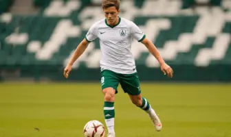 Young midfielder in white and green kit dribbling football on professional pitch