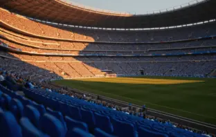 Floodlit football stadium at golden-hour kick-off with packed stands, dramatic shadows on empty pitch, Argentina and Egypt national colours.