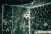 Football striking Champions League net under green stadium lights with crowd in background