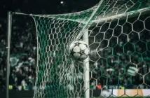 Football striking Champions League net under green stadium lights with crowd in background