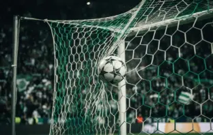 Football striking Champions League net under green stadium lights with crowd in background