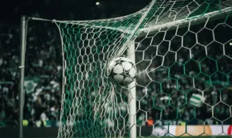 Football striking Champions League net under green stadium lights with crowd in background