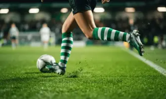 Female footballer in green and white hooped socks sprinting with ball on pitch