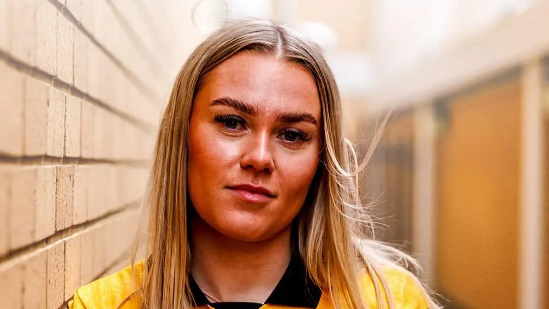 A woman in a yellow football jersey stands in a corridor.