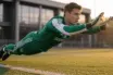Young goalkeeper in Celtic green making athletic diving save during training at professional football facility