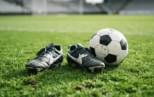 Football boots and ball on green pitch representing striker recruitment opportunity