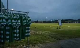 Empty Celtic training ground at dusk with unused hooped jerseys on rack, evoking summer transfer uncertainty