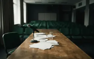 Empty boardroom table with microphone and scattered papers in moody dramatic lighting