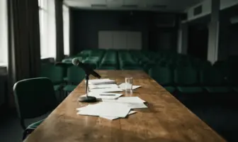 Empty boardroom table with microphone and scattered papers in moody dramatic lighting