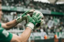 Goalkeeper gloves catching football with Celtic green and white stadium background
