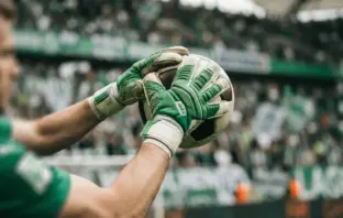 Goalkeeper gloves catching football with Celtic green and white stadium background
