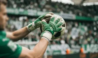 Goalkeeper gloves catching football with Celtic green and white stadium background