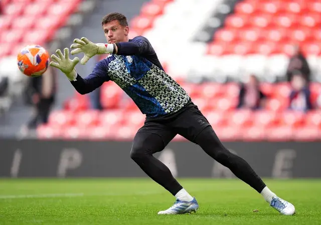 Goalkeeper Dinko Horkas in a blue and black patterned jersey catching a soccer ball during a match