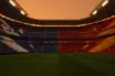 Floodlit stadium at sunset with blue and red-gold crowd sections creating dramatic lighting contrast.