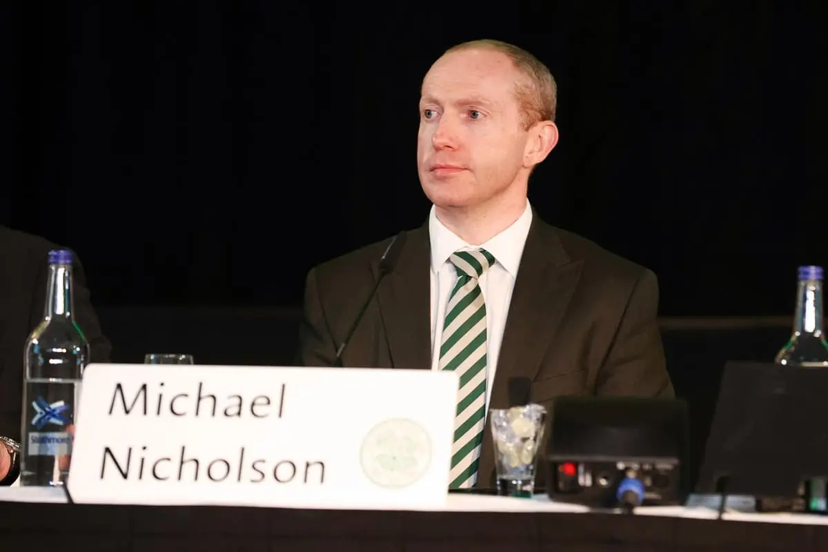 Michael Nicholson sitting at a conference table with a nameplate and water bottles.
