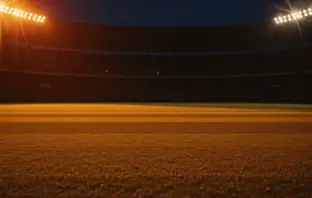 Empty floodlit stadium pitch at golden hour with dramatic shadows, warm amber and red lighting, packed stands silhouetted against night sky.