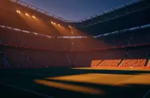 Floodlit stadium at golden hour with packed stands, dramatic shadows, Swiss red and Colombian colours in atmospheric haze.