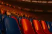 Close-up of blue and red stadium seats under golden-hour floodlights, packed stands in atmospheric bokeh.
