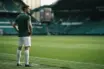Celtic-style centre-back standing on a hybrid grass pitch ahead of an away match
