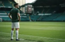 Celtic-style centre-back standing on a hybrid grass pitch ahead of an away match