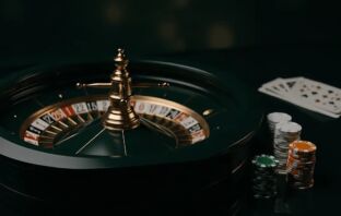 Green and white roulette wheel with Celtic-green casino chips on a dark reflective table, cinematic casino lighting.