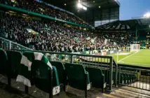 Green-and-white scarf in a floodlit stadium representing Celtic’s Champions League opportunity and potential revenue.