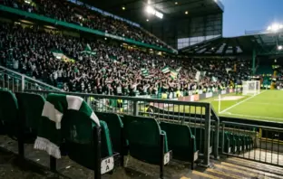 Green-and-white scarf in a floodlit stadium representing Celtic’s Champions League opportunity and potential revenue.
