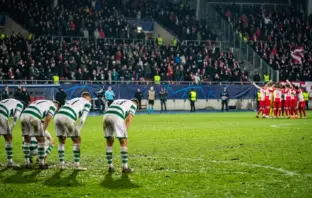 Dejected Celtic-inspired players react after a dramatic European football collapse in a floodlit stadium