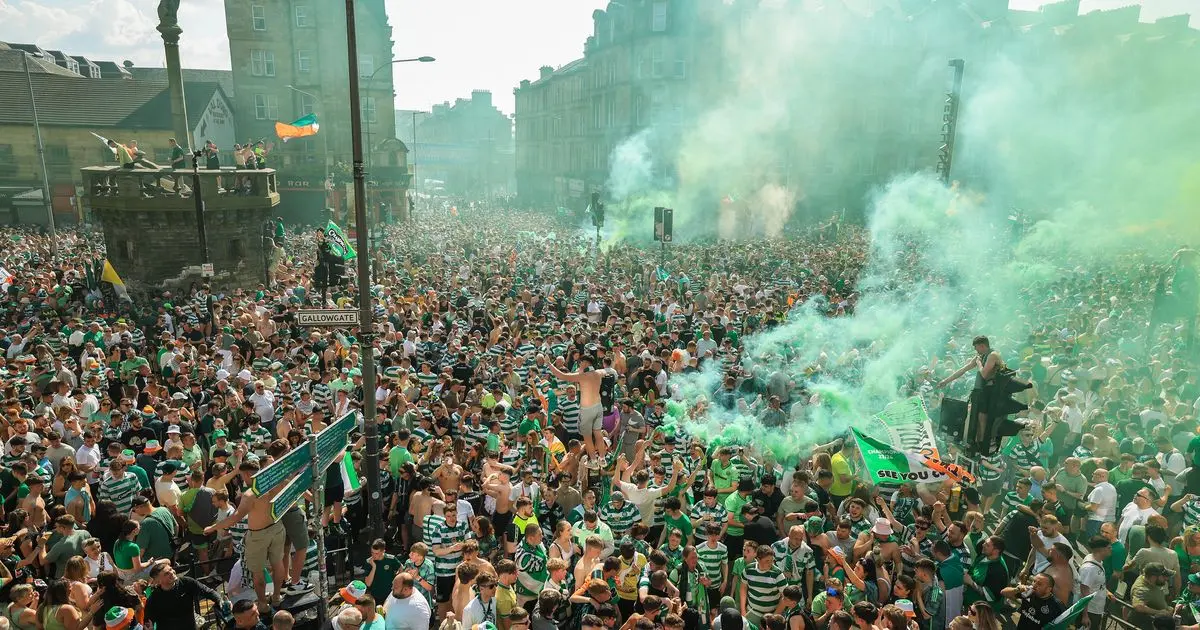 Crowds of Celtic FC fans in green and white hoops celebrating at Glasgow Cross with green smoke flares.