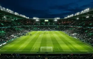 Floodlit football stadium at night with emerald green pitch and atmospheric green lighting in the stands