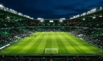 Floodlit football stadium at night with emerald green pitch and atmospheric green lighting in the stands