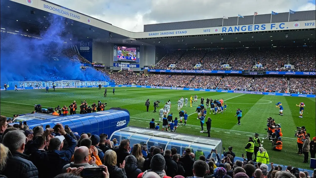 Wide view of Ibrox Stadium with Rangers F.C. signage, players on the pitch, and fans in the stands.