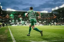 Celtic left-back sprinting down the wing to deliver a cross in packed stadium at twilight