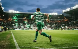Celtic left-back sprinting down the wing to deliver a cross in packed stadium at twilight