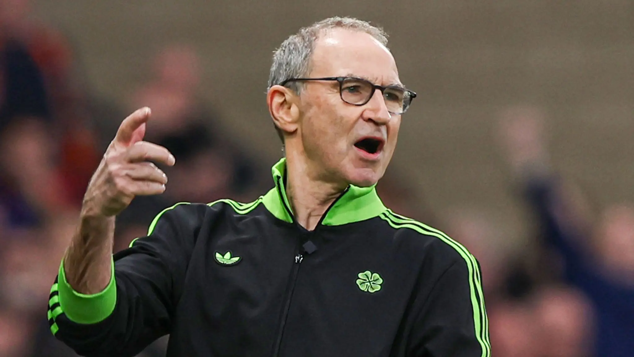 Martin O'Neill wearing a black and green Celtic FC tracksuit and glasses, gesturing on the sidelines.