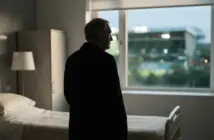 Respectful silhouette of a football manager near a hospital window with a softly lit stadium beyond