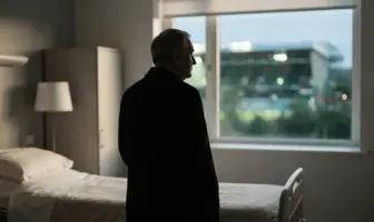 Respectful silhouette of a football manager near a hospital window with a softly lit stadium beyond