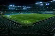 Stadium clock showing added time beyond 45 minutes with yellow card on pitch under floodlights