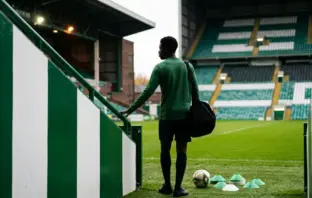 Young midfielder in green training kit arriving at a football stadium for a new club chapter