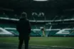 Non-identifiable football manager overlooking a green-lit stadium amid Celtic financial pressure