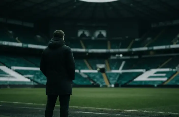 Non-identifiable football manager overlooking a green-lit stadium amid Celtic financial pressure
