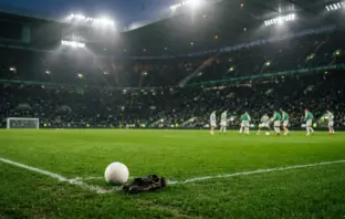 Empty left wing on a floodlit football pitch symbolising Celtic's squad depth test without Yang Hyun-jun